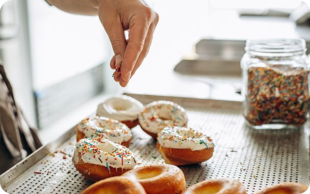 A hand sprinkles raisins on a donut